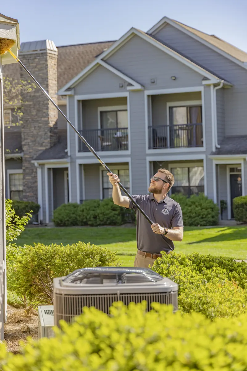Berner Pest Solutions technician dewebbing high exterior eaves with an extension pole during a spider treatment